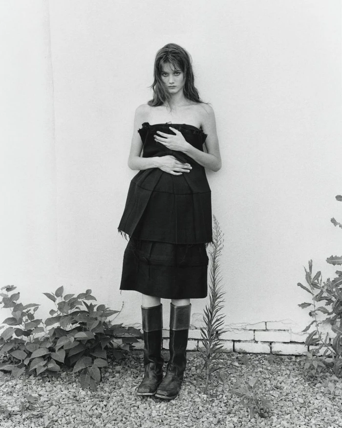 Model in a black strapless dress and tall boots standing against a wall for The Courtyard project by Crosscurrent