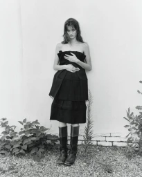 Model in a black strapless dress and tall boots standing against a wall for The Courtyard project by Crosscurrent