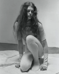 Black and white portrait of a female model crouching on a draped canvas surface in a minimalist studio.