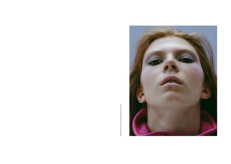 Close-up portrait of a fair-skinned adult female with auburn hair, wearing makeup and a pink collar, set against a light blue backdrop.
