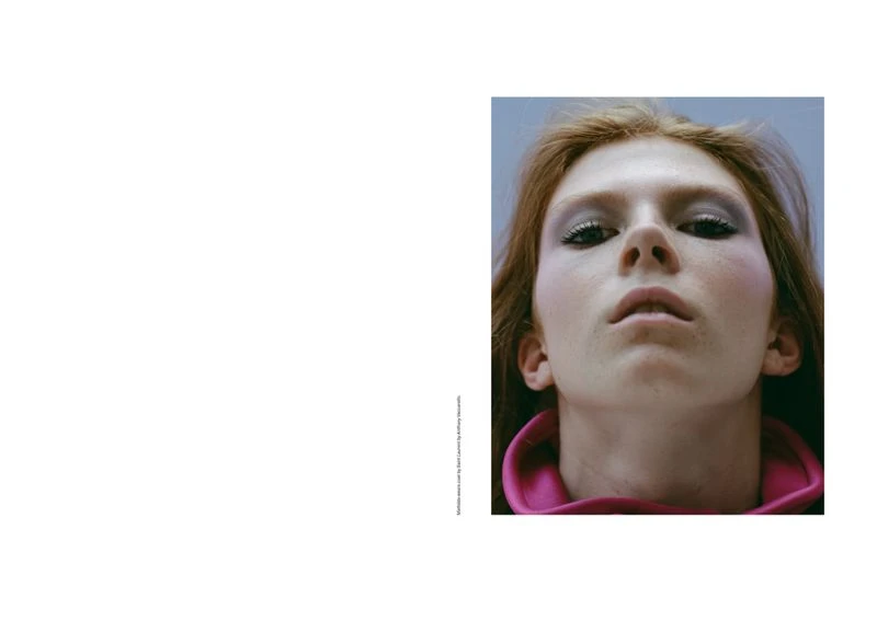Close-up portrait of a fair-skinned adult female with auburn hair, wearing makeup and a pink collar, set against a light blue backdrop.
