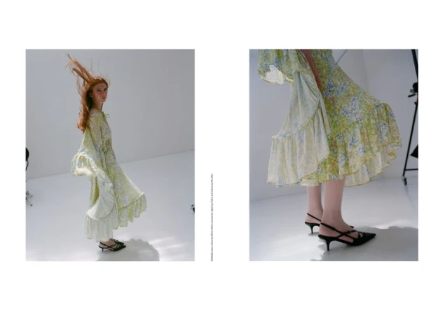 A woman wearing a floral dress poses in a bright photo studio, showcasing a full-body fashion shot with her auburn hair flying in the air.