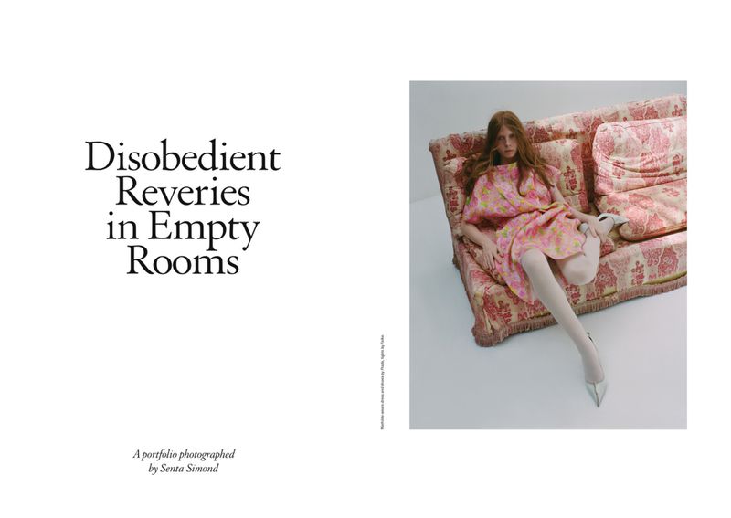 A red-haired woman in a pink floral dress and heels sits on a pink floral sofa against a white background in a fashion editorial photo.