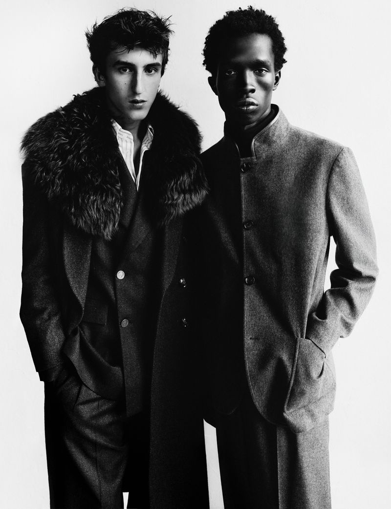 Two male models in dark tailored coats posing against a plain white background for Harper's Bazaar France Homme.