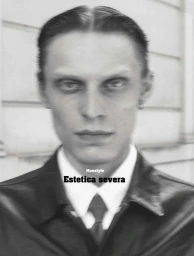 Monochrome portrait of a man in a dark jacket, white shirt, and tie against a building exterior wall.