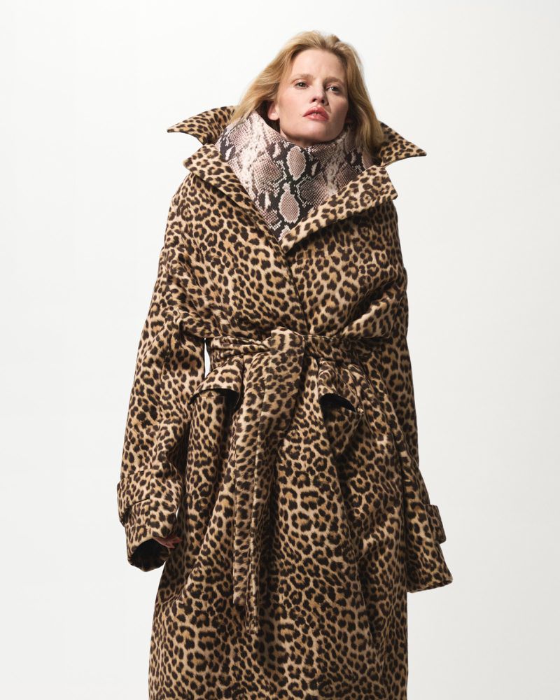 Adult woman wearing a long animal print coat with a snake skin print turtleneck in a studio setting. Fashion editorial portrait.