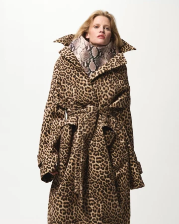 Adult woman wearing a long animal print coat with a snake skin print turtleneck in a studio setting. Fashion editorial portrait.