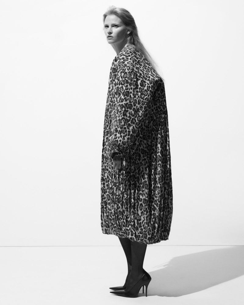Black and white fashion shot of a woman wearing a leopard print coat and black heels, standing in front of a plain background.