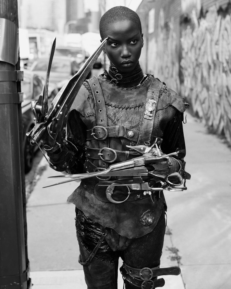 Striking black and white portrait of a slender woman in a creative, belted, Edward Scissorhands-inspired costume, standing outdoors.