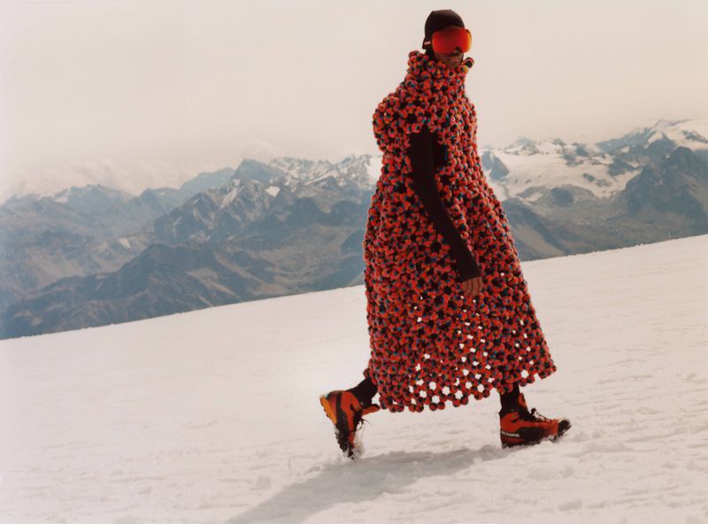 A person wearing an orange floral coat and goggles walks on snow-covered mountain. Dramatic and unique fashion statement in snowy landscape.