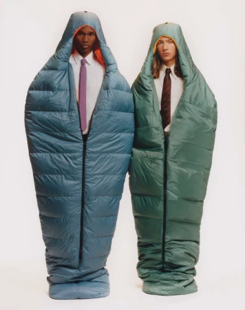 Two men in teal and green sleeping bags standing side-by-side in front of a plain white background, wearing ties and collared shirts.