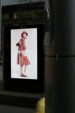 Outdoor advertising billboard featuring a stylish woman in a red plaid outfit and hat for Oroton, showcasing fashion and urban advertising.