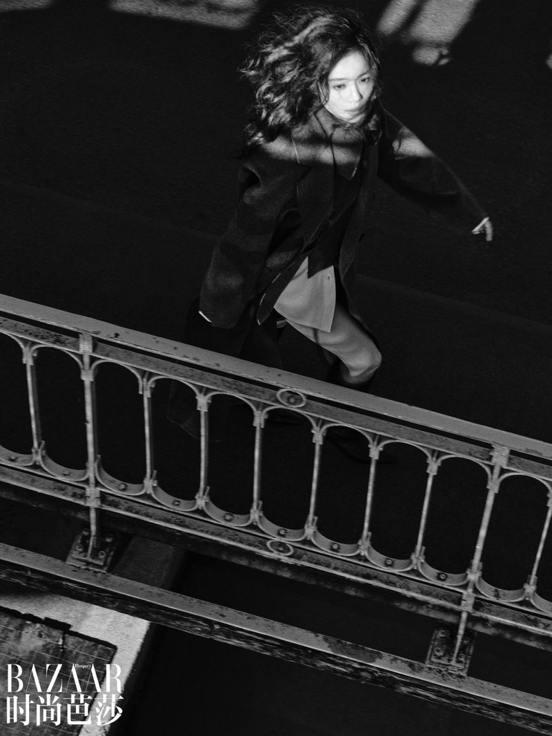 Model walking past a decorative metal bridge railing in a black and white fashion editorial for Harper's Bazaar China.