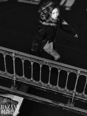 Model walking past a decorative metal bridge railing in a black and white fashion editorial for Harper's Bazaar China.
