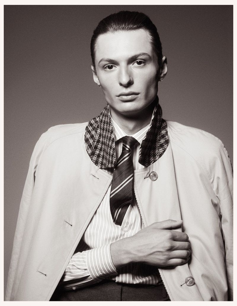 Portrait of a male model wearing a striped shirt, patterned collar jacket, and tie against a plain grey studio backdrop
