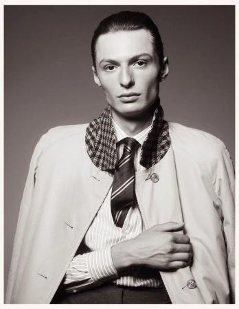 Portrait of a male model wearing a striped shirt, patterned collar jacket, and tie against a plain grey studio backdrop