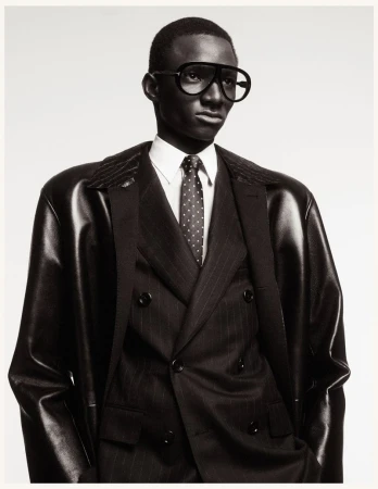 Portrait of a Black man in a pinstripe suit and aviator glasses, posing against a white backdrop in a studio, fashion photography.