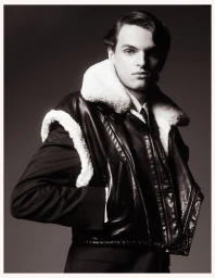 A male model wearing a dark leather jacket with white shearling collar posing against a dark background