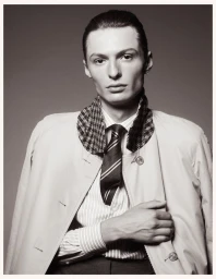 Portrait of a male model wearing a striped shirt, patterned collar jacket, and tie against a plain grey studio backdrop