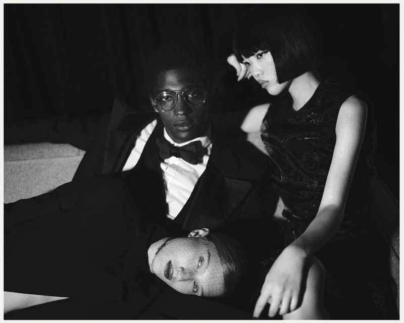Monochrome portrait featuring three fashionably dressed individuals: an African-American man in a suit and two Asian women in dresses.