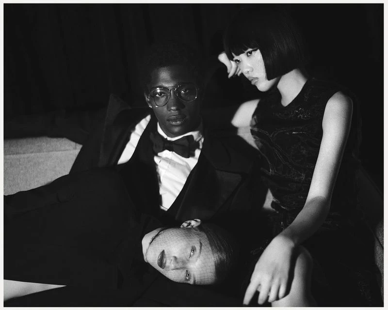 Monochrome portrait featuring three fashionably dressed individuals: an African-American man in a suit and two Asian women in dresses.