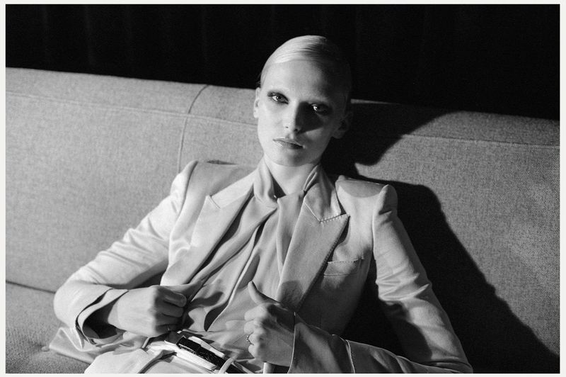 Striking black and white fashion portrait of a slender woman in a blazer sitting on a couch, exuding minimalist elegance.
