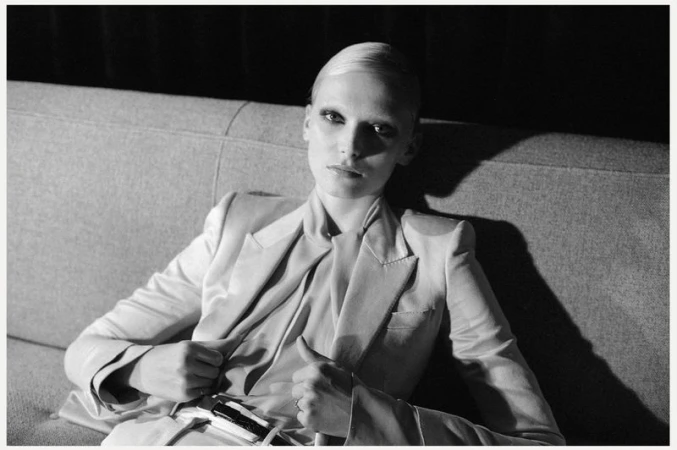 Striking black and white fashion portrait of a slender woman in a blazer sitting on a couch, exuding minimalist elegance.