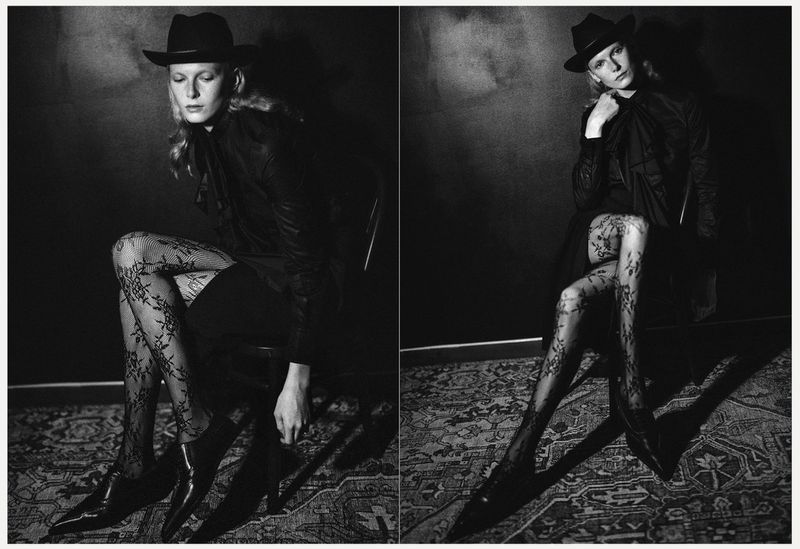 Monochrome portrait of a young woman in a hat and patterned tights sitting in a chair against a dark textured background in a photo studio.
