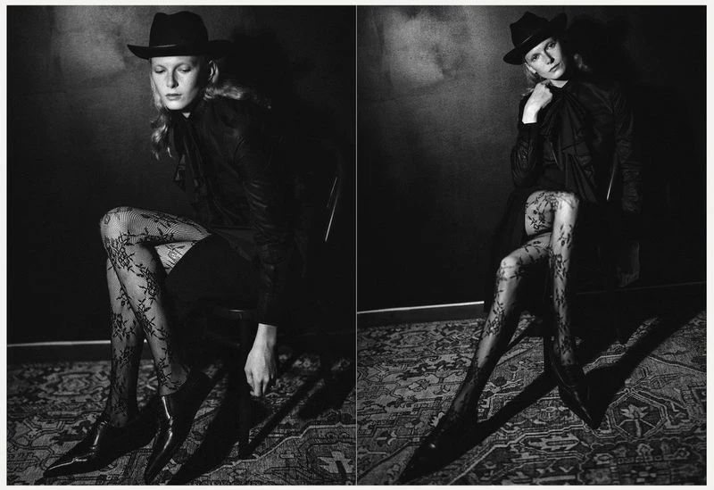 Monochrome portrait of a young woman in a hat and patterned tights sitting in a chair against a dark textured background in a photo studio.