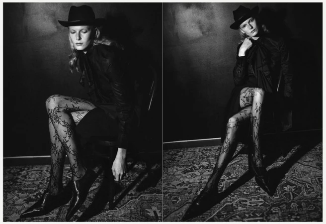 Monochrome portrait of a young woman in a hat and patterned tights sitting in a chair against a dark textured background in a photo studio.