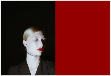 Portrait of a blonde model with red lipstick and dark jacket against a dark background split with a bold red section.