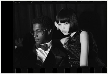 Black and white portrait of a man in glasses and a woman with dark hair posing together for Rouge Fashionbook