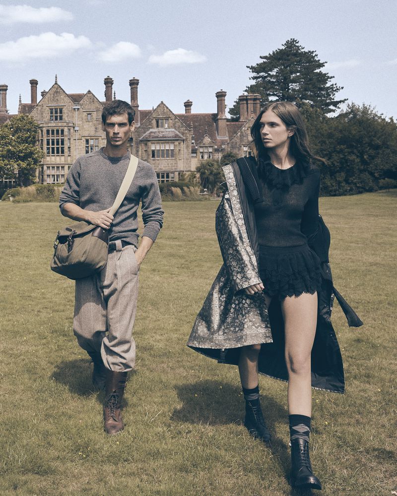A vintage-style fashion shot outdoors features a male and female model walking on a lawn in front of a historic building.