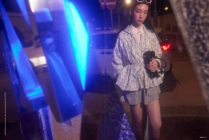 Fashion shot of an Asian woman posing at night, wearing a floral jacket and grey shorts, accessorized with a handbag and white sunglasses.