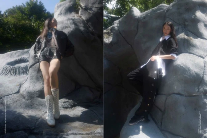 Two Asian women in stylish, dark-colored outfits pose on rocks under a sunny sky, creating a fashionable outdoor editorial scene.