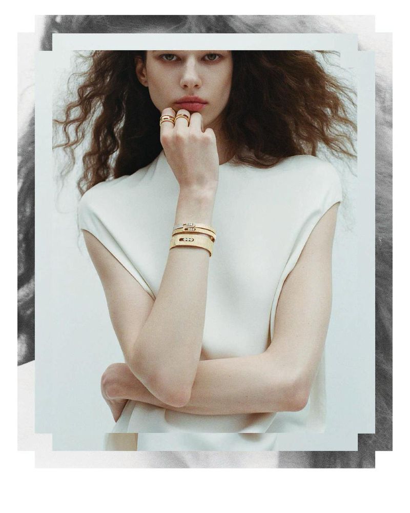 Model wearing gold rings and stacked bangles with a white sleeveless top against a light background