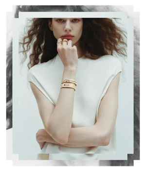 Model wearing gold rings and stacked bangles with a white sleeveless top against a light background