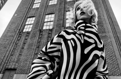 Model wearing a black and white patterned coat looking up against a brick building exterior