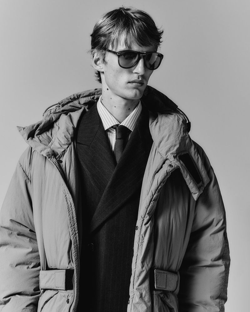 Model wearing dark sunglasses, suit jacket, and puffer coat against a plain background for Esquire Italia