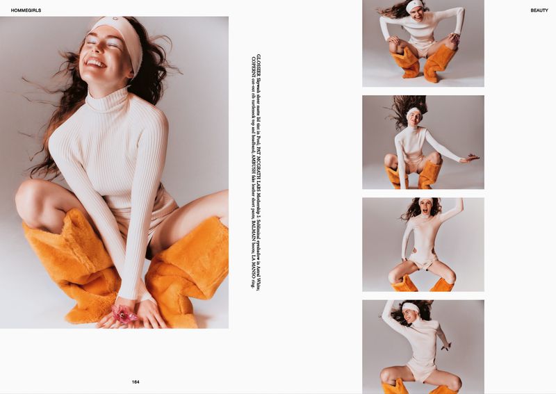 Smiling woman in studio wearing beige turtleneck and orange furry boots, holding flowers. Beauty and fashion editorial shot.