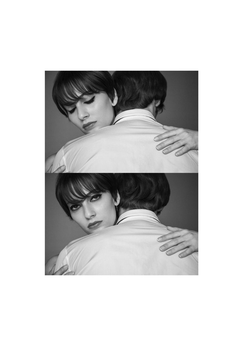 Black and white studio shot featuring a woman with bangs embracing a person, both wearing collared shirts against a solid backdrop.