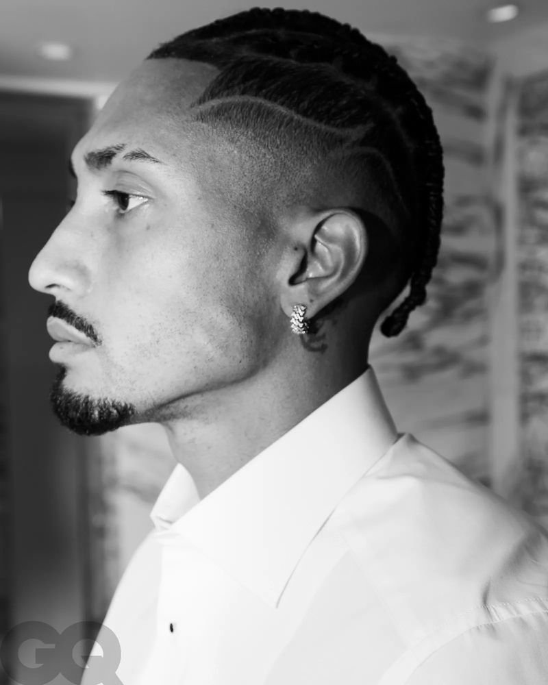 Monochrome portrait of a stylish adult male with unique braided hairstyle, wearing a white dress shirt and hoop earring.