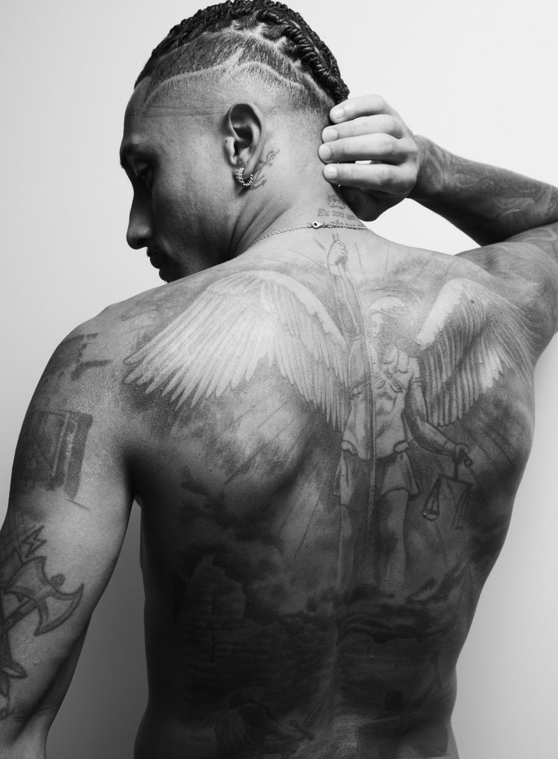 Monochrome portrait of athlete Raphinha showing extensive angel tattoo on his back and braided hair, shot by Alan Gelati for GQ España.