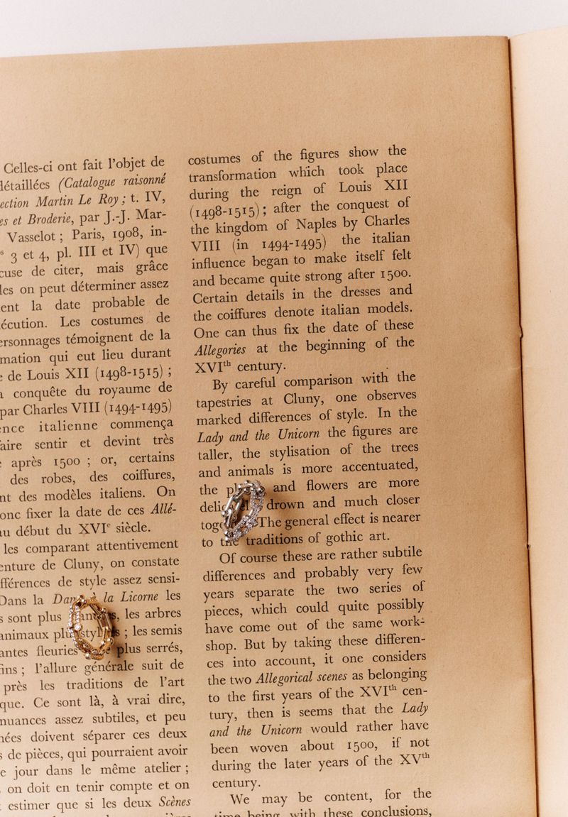 Close-up of gold and silver vintage earring sets on a book page with detailed text about fashion and tapestry traditions.