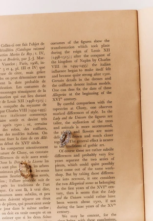 Close-up of gold and silver vintage earring sets on a book page with detailed text about fashion and tapestry traditions.