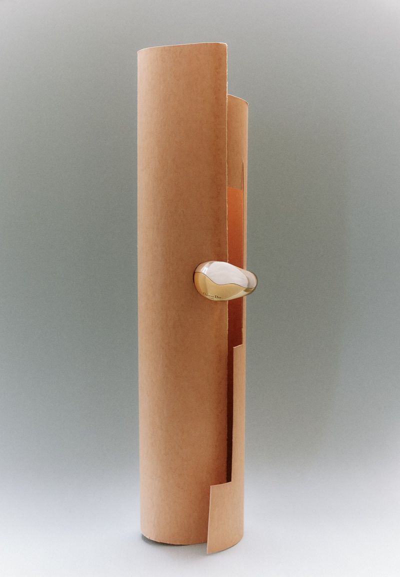 Abstract shot of a peach-colored scroll-like cylinder with a metallic, rounded accent, set against a plain gray backdrop, minimalist design.