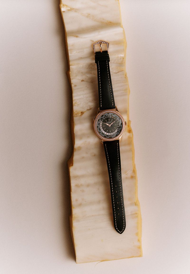 Close-up of a women's wristwatch with a black strap and rose gold accents on a textured marble surface. Studio lighting, product photography.