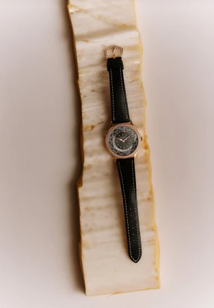 Close-up of a women's wristwatch with a black strap and rose gold accents on a textured marble surface. Studio lighting, product photography.
