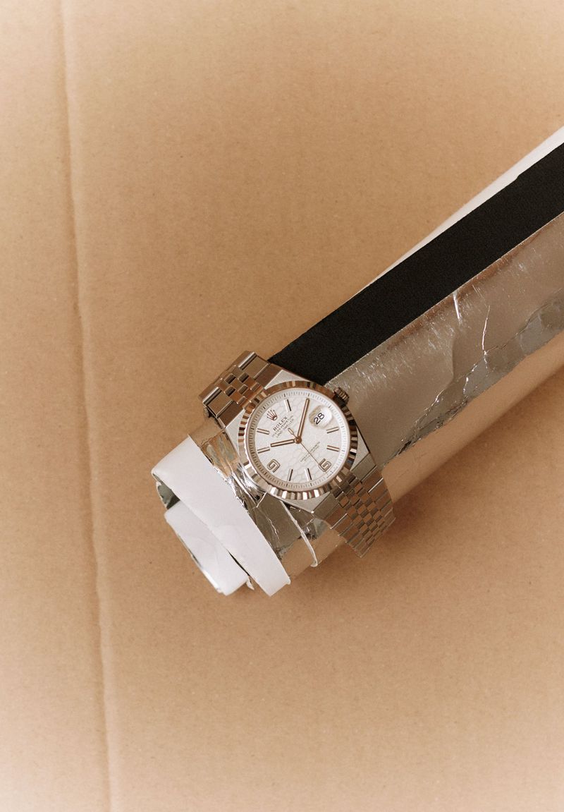 Wristwatch on a silver tube against a beige backdrop, showcasing its dial, band, and design, simple composition.