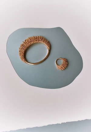 Two textured gold beaded rings displayed on an organic slate grey shape over a light background for Z Magazine